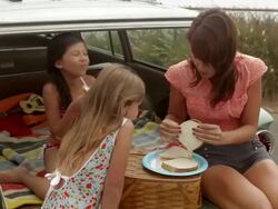 Mother and daughters sitting on car eating sandwiches Stock Footage