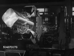 1952: CANADA: ALUMINUM INDUSTRY: Alcan (Aluminum Company of Canada) robotic arm lifting large square shaped block, pulling back, placing into shaping machine, top pressing uniform dents. CU Stacked bars on loader, moving back REVEALS stacks of bars. Instructional Video
