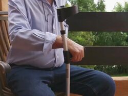 Senior male leaves patio chair aided by crutch Stock Footage
