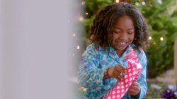 Smiling parents watch as girl unwraps Christmas present (dolly-shot) Stock Footage