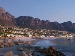 T/L Camps Bay beach and Twelve Apostle Mountains with Tide going out and town lighting up as night falls, Cape Town, South Africa Stock Footage