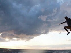 A young man jumping off a wall during sunset at the beach. - Model Released - HD Stock Footage