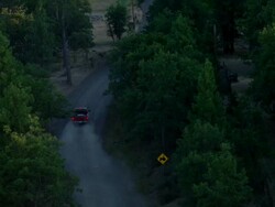 Red pickup truck driving a gravel road through trees Stock Footage