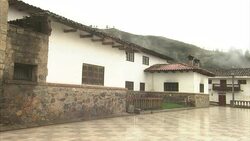 A large Peruvian adobe and stone  building stands behind a low wall on a plaza. Stock Footage