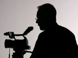 Videographer Cameraman Adjusts Camera, Directs; Silhouette Stock Footage