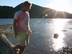 Man hops onto log at mtn lake edge, balances, sunrise Stock Footage