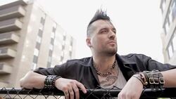 Pensive cool young man with mohawk leaning on fence looking away below urban buildings Stock Footage