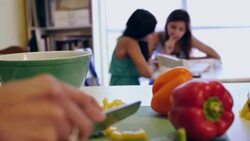 Preteen girl doing homework while big sister tutors her and mother prepares dinner Stock Footage