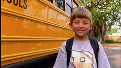 A young boy holds an apple and smiles in front of his school bus. Stock Footage