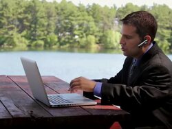 MS Man sitting on table and talking on bluetooth while typing on laptop near lake / Portland, ME, United States Stock Footage