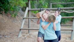 Teams racing with logs on boot camp obstacle course Stock Footage