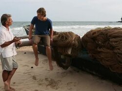Pan to father and son having conversation by boat, at beach Stock Footage