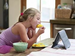 MS Shot of young girl eating and watching her tablet in her kitchen / Lamy, New Mexico, United States Stock Footage