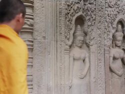 MS A Buddhist monk walks past looking at intricate stone carvings in an ancient temple in Angkor Wat / Siem Reap, Cambodia Stock Footage