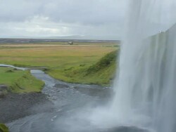 MS PAN Shot of waterfall crashing on ground with grassy landscape and people looking on below / Vestmannaeyjar, Sudhurland, Iceland Stock Footage