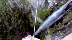 Man traverses highline stretched above waterfall, valley Stock Footage