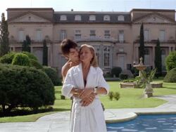 Wide shot mature woman and young man embracing on pool deck outside her mansion / kissing / smiling at CAM Stock Footage