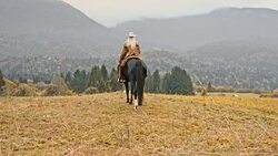 SLO MO Herdswoman riding her horse across mountain meadow Stock Footage
