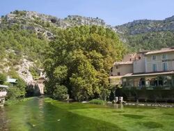 WS PAN View of houses and water wheel moving on River Sorgue with mountain / Fontaine de Vaucluse, Vaucluse, France Stock Footage