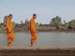 MS Buddhist monks walk along the edge of a moat with Angkor Wat temple in the background / Siem Reap, Cambodia Stock Footage