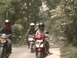 Motorbikers ride along ash covered road wearing masks, Indonesia 28 October 2010 / AUDIO Stock Footage