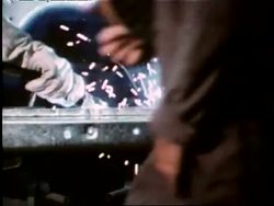 A steel worker stokes a furnace as sparks fly; an auto worker welds car parts in a factory. News Clip
