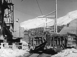 1952: CANADA: HYDROELECTRIC POWER: TU Mountainside. AERIAL: Mountains. VS Small railroad ore cars coming out of snow covered mountain tunnel. VS Construction workers using high-pressure hoses on fill rocks, dump truck dumping rocks mountainside. Instructional Video