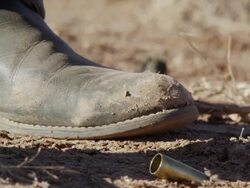 Up close view of cowboy boots as bullet shells fall to the ground next to them. Stock Footage