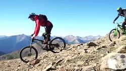 Mountain bikers descend steep mountain slope, from summit Stock Footage