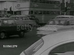 1966: GERMANY: CITYSCAPE: VS Cars traveling on busy city road, Volkswagens, Mercedes, motorcycle, VS People walking, crowded sidewalks, people wearing coats walking, crossing street intersection, many middle-aged. Instructional Video