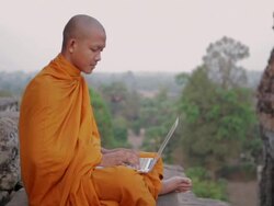 MS, PAN A Buddhist monk types on a laptop computer and pauses to think, on top of an ancient temple in Angkor Wat / Siem Reap, Cambodia Stock Footage