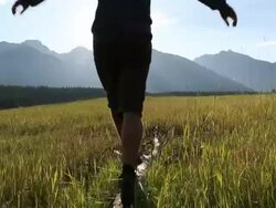 Pan as teenage boy balances on log in mtn meadow Stock Footage