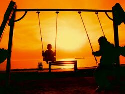 Silhouettes of children on a swing at sunset Stock Footage