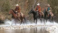 SLO MO DS Three ranchers crossing river on galloping horses Stock Footage