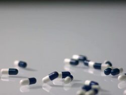 High speed Blue and white capsule pills fall on to reflective white surface Stock Footage
