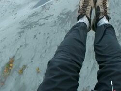 High Angle hand-held - A pair of legs hang in the air as they drift over a mountainous landscape / Alaska, USA Stock Footage