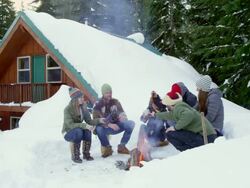 MS group of friends sitting around fire in front of cabin in snow toasting with beverages. Stock Footage