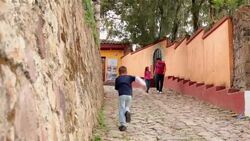 Hispanic brother and sister hold hands walking down third-world street, young boy runs by Stock Footage