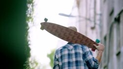 Young man walks through downtown alley carrying longboard over shoulder Stock Footage
