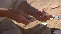 A pair of hands picks up shards of pottery and glass in a desert. Stock Footage
