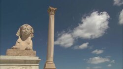 Fluffy white clouds drift over a Sphinx and a solitary column in Cairo. Stock Footage