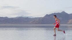 MS PAN Male athlete sprinting across lake with mountain range in background Stock Footage