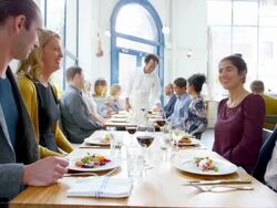 MS laughing couples dining together in restaurant with waiter clearing plates from table in background Stock Footage