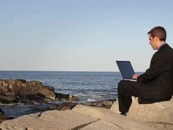 MS Man sitting on rocks while typing on laptop at ocean / Portland, ME, United States Stock Footage