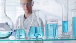 Scientist writing on clipboard behind variety of beakers Stock Footage