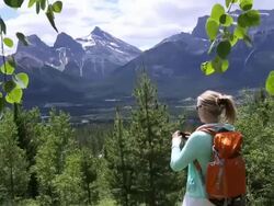 Pan of hiker walking into forest, takes picture of mtns Stock Footage