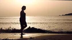 Young woman walking on sea shore during sunset Stock Footage