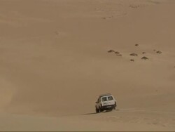 Medium Long Shot, tracking-left - A vehicle drives down a steep sand dune in the Sahara Desert in Egypt Stock Footage