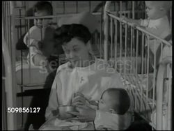 1946: NEW YORK FOUNDLING HOSPITAL: EXT N.Y. Foundling Hospital. HA Long double row of Nursery booths. Nurse holding, feeding formula to baby, turning to talk two babies in cribs BG. Nurse feeding orphan baby bottle, putting baby on shoulder, burping. Instructional Video