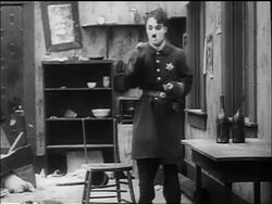 B/W 1917 cop Charlie Chaplin takes cigarette, sits down, leans back on backless chair + falls over Stock Footage